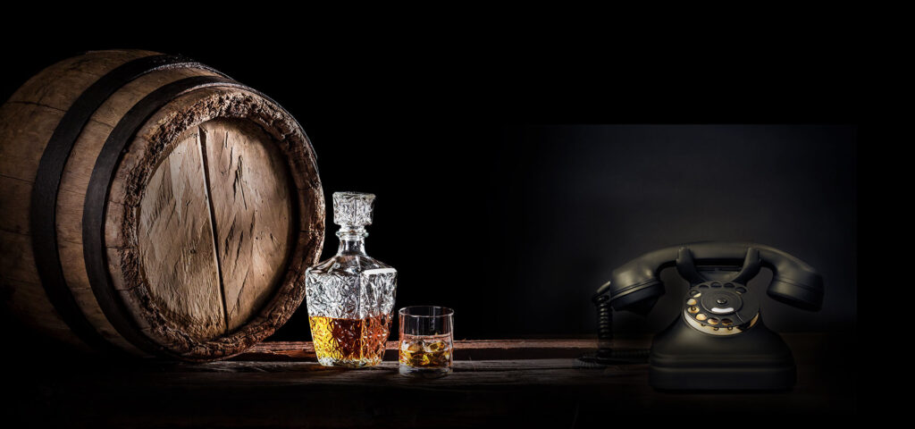 Whisky decanter with glass beside an oak barrel and vintage rotary telephone – investor contact Associated Alcohols